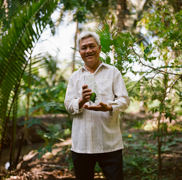 A portrait of one of Real Coco's producers, holding a tetra pack of Real Coco Coconut Water. Scene is set in a forest in Vietnam.